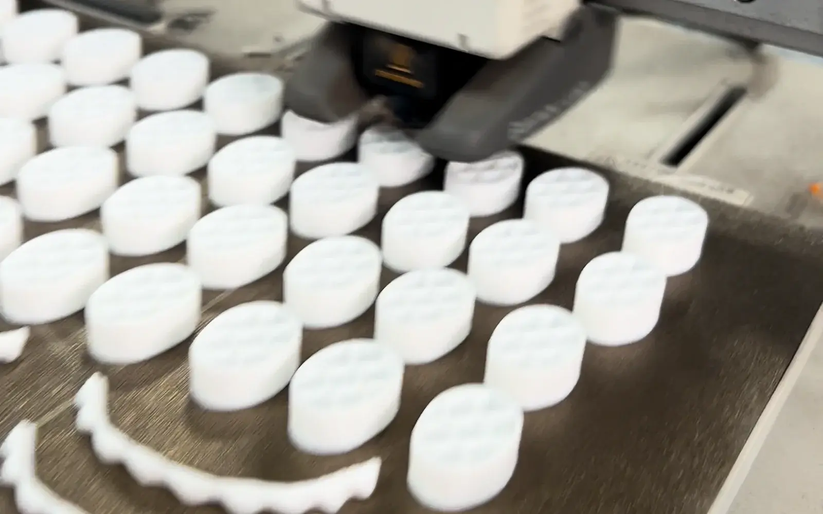 Multiple matching white parts arranged across a printer build plate