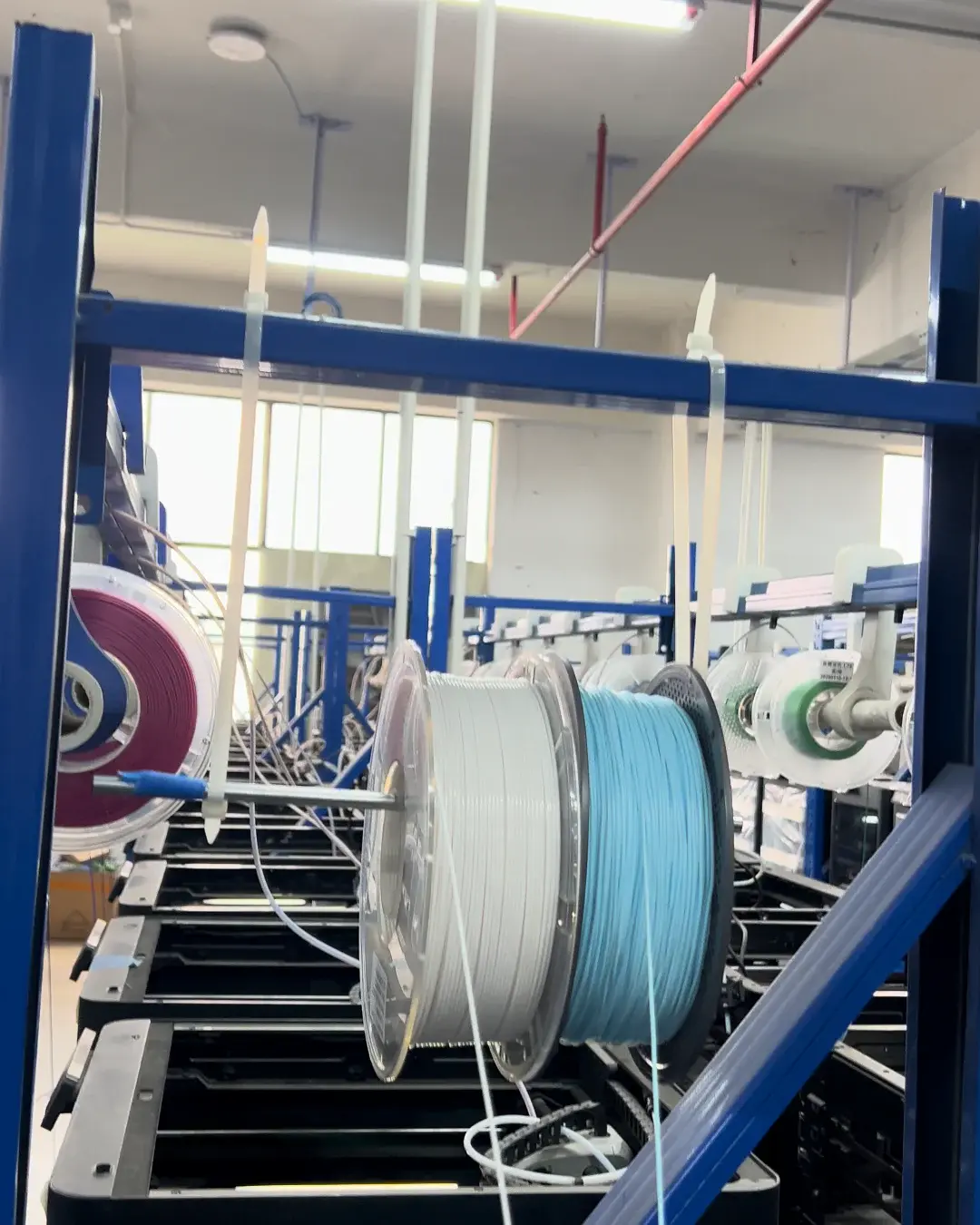 Filament spools routed to FDM printers in a production rack